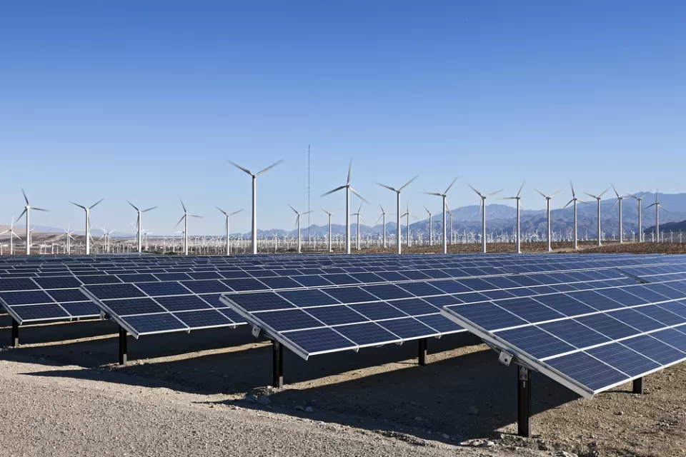 Solar array and wind turbines in California with mountains in background